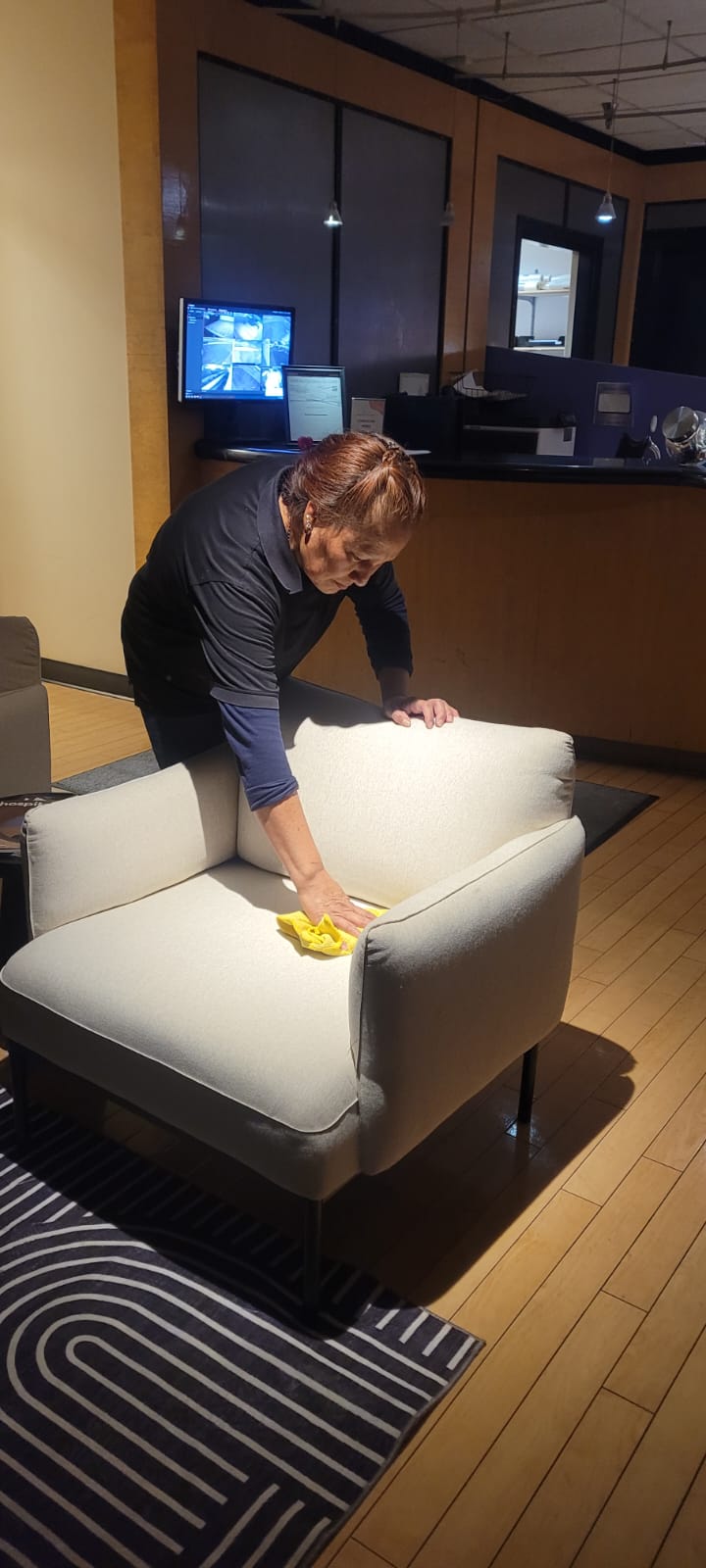 Woman cleaning a beige armchair with a yellow cloth in a modern indoor setting.